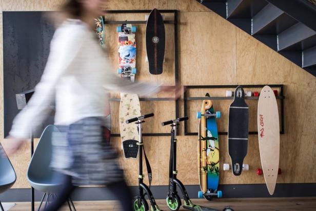 Eine Frau geht an einer Wand mit Skateboards und Rollern vorbei.