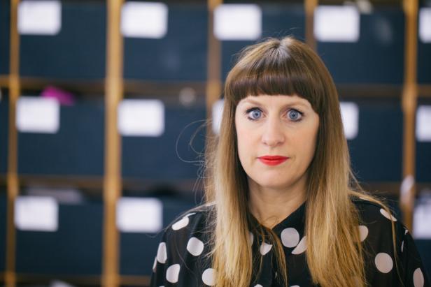 Eine Frau mit Ponyfrisur und rotem Lippenstift blickt in die Kamera.