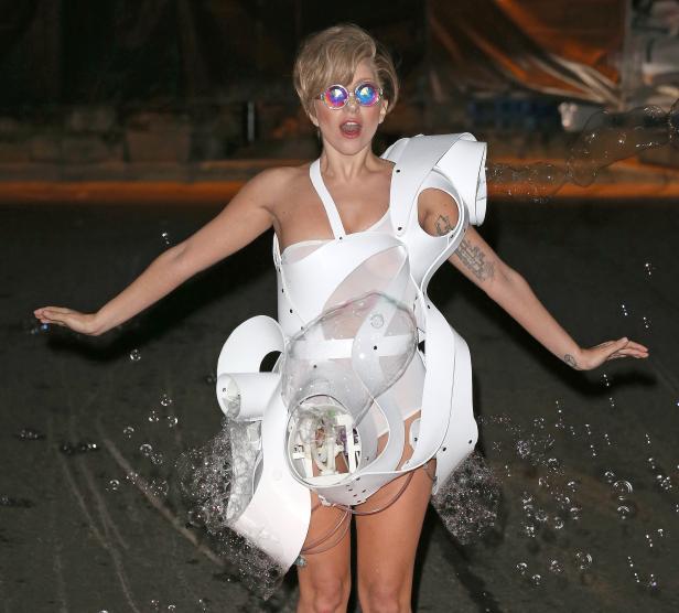 Lady Gaga in einem weißen, futuristischen Kostüm, umgeben von Seifenblasen.