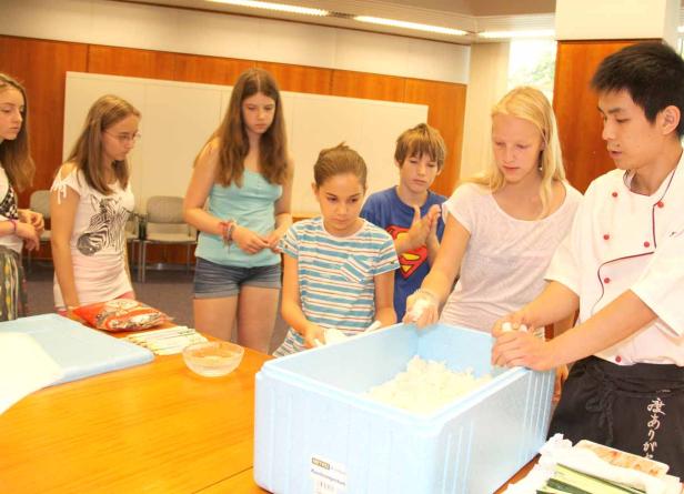 Eine Gruppe Jugendlicher lernt von einem Koch, wie man Sushi zubereitet.