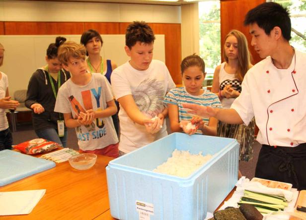 Eine Gruppe von Kindern lernt von einem Koch, wie man Sushi zubereitet.