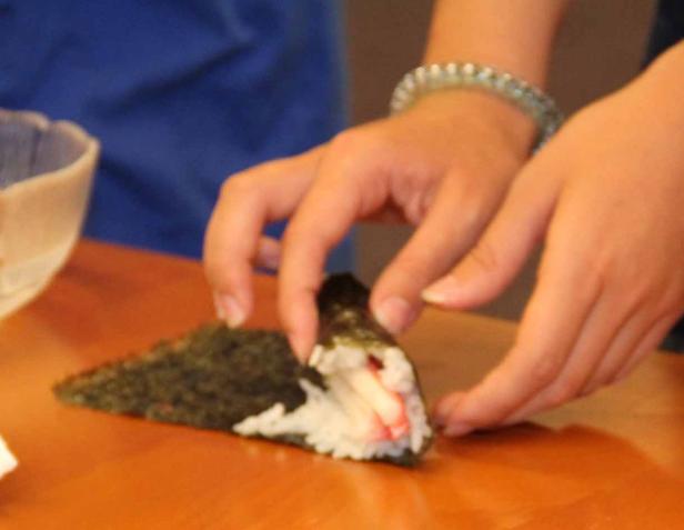 Eine Person bereitet eine Temaki-Sushi-Rolle zu.