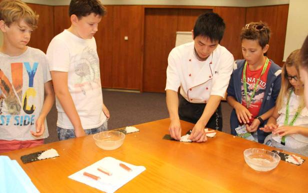 Ein Koch zeigt einer Gruppe von Kindern, wie man Sushi zubereitet.