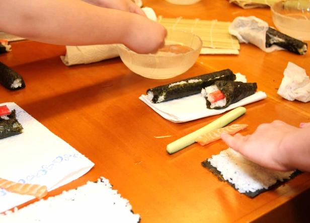 Zwei Personen bereiten Sushi auf einem Holztisch zu.