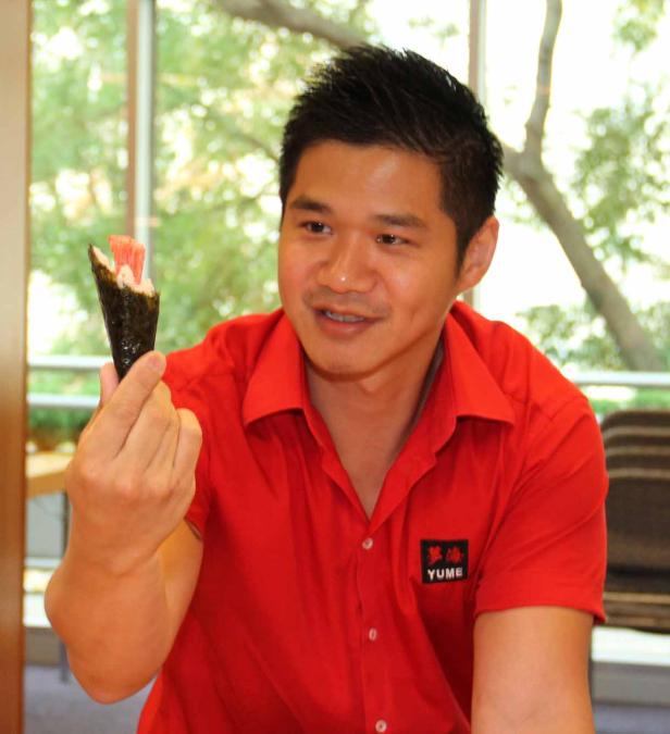 Ein Mann im roten Hemd hält eine Temaki-Sushi-Rolle hoch.