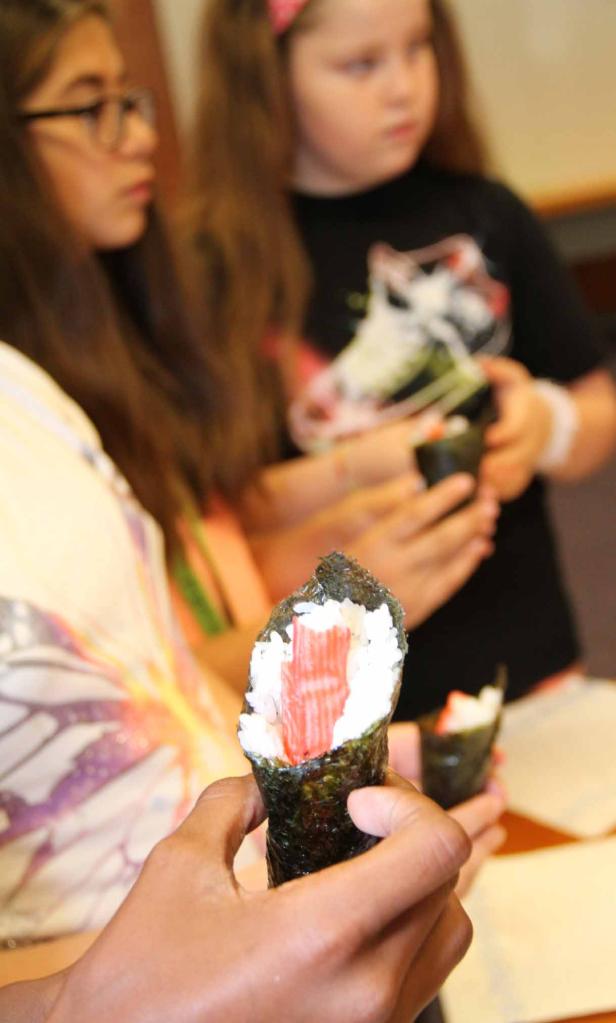 Eine Person hält ein Temaki-Sushi mit Krabbenfleisch in der Hand.