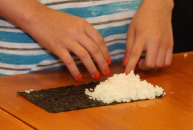 Eine Person belegt ein Noriblatt mit Reis, um Sushi zuzubereiten.