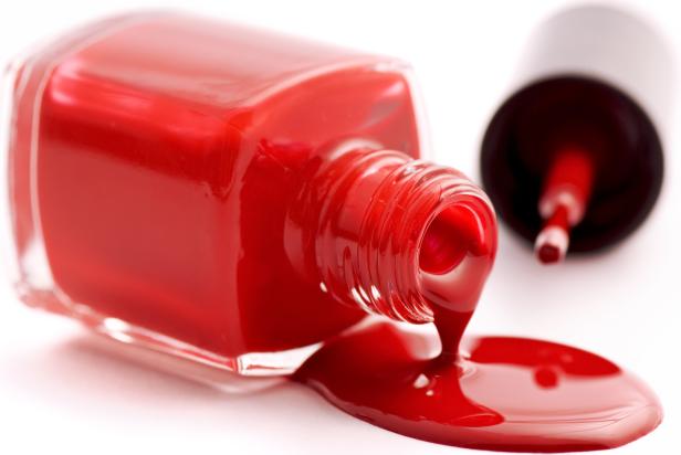 Eine geöffnete Flasche roter Nagellack liegt auf der Seite und verschüttet Farbe.