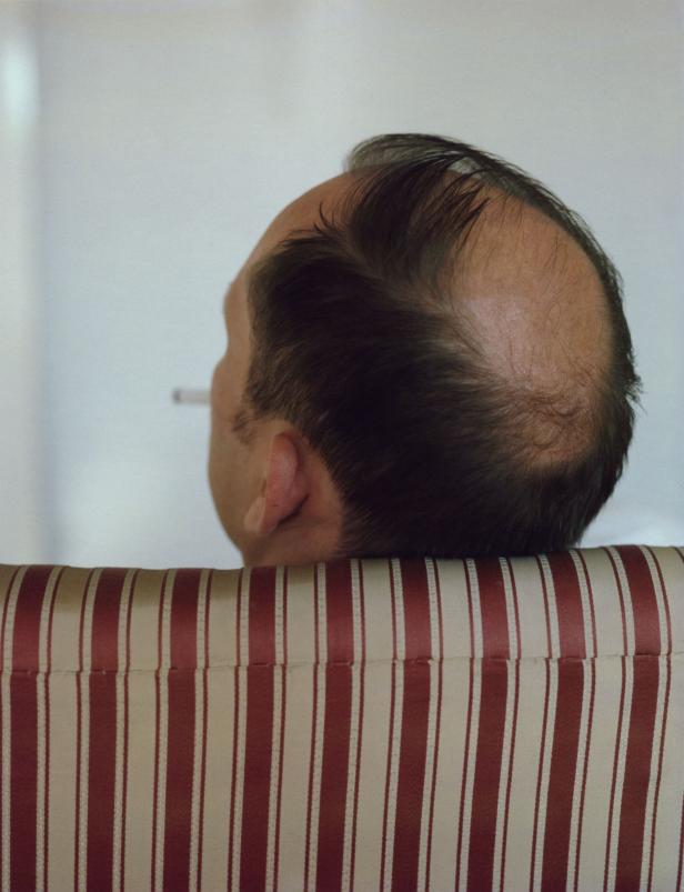Ein Mann sitzt mit dem Rücken zur Kamera und raucht eine Zigarette.