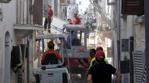 Die Rettungsmannschaften suchen nach weiteren möglichen Opfern. In einer engen Gasse räumen Arbeiter Trümmer mit kleinen Baggern weg.