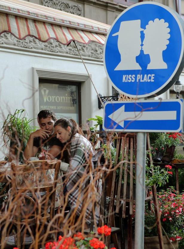 Ein Paar sitzt an einem Tisch in einem Café unter einem Schild mit der Aufschrift „Kiss Place“.