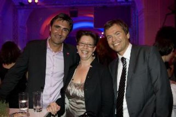 Drei Personen posieren lächelnd für ein Foto bei einer Veranstaltung.