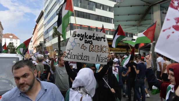 Eine Demonstration mit Palästina-Flaggen und einem Schild mit der Aufschrift „Boykottiert das 4. Reich. Zionisten = Nazis“.
