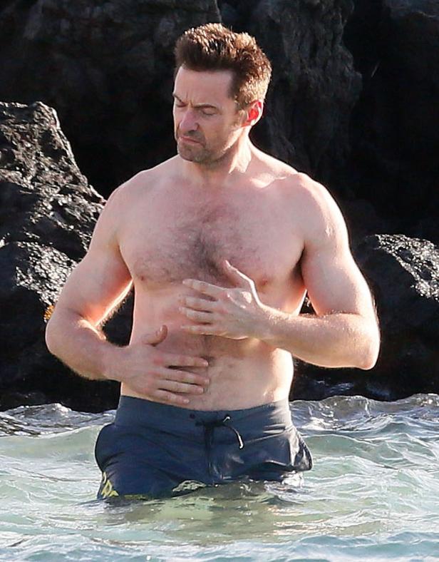 Hugh Jackman steht im Wasser und hält sich den Bauch.