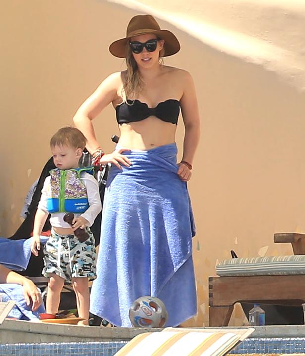 Eine Frau mit Hut und ein Kind mit Schwimmweste stehen am Pool.