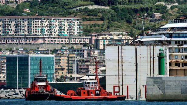 Zwei rote Schlepper stehen vor dem teilweise abgewrackten Kreuzfahrtschiff Costa Concordia.