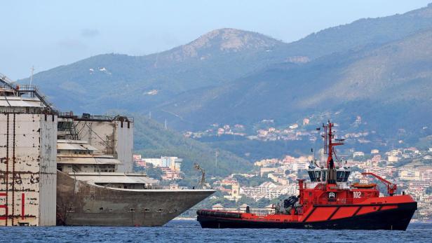 Ein roter Schlepper neben dem teilweise versunkenen Wrack der Costa Concordia vor der Küste Italiens.