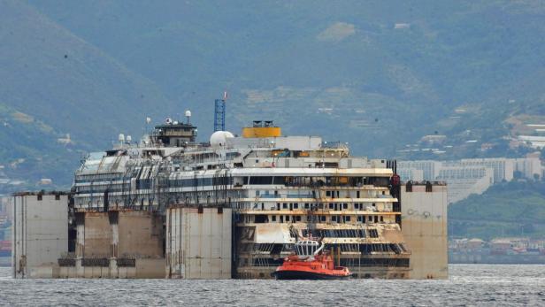 Das halb versunkene Kreuzfahrtschiff Costa Concordia mit einem Schlepper daneben.