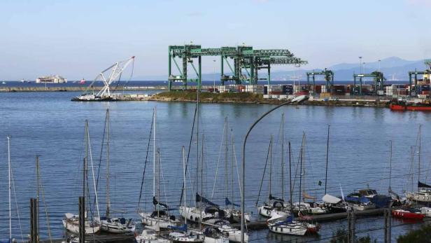 Blick auf einen Hafen mit Segelbooten im Vordergrund und einem Containerterminal im Hintergrund.