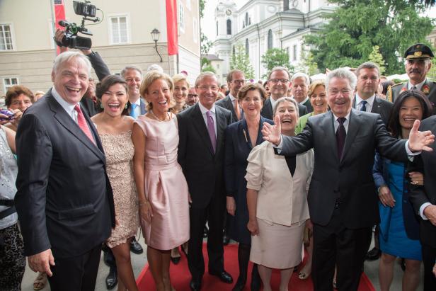 Eine Gruppe von Menschen posiert lachend auf einem roten Teppich vor einem Gebäude in Salzburg.