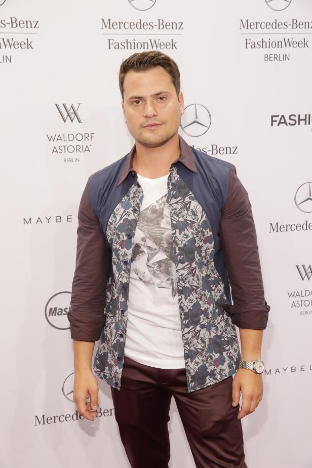 Ein Mann posiert vor einem Hintergrund der Mercedes-Benz Fashion Week Berlin.