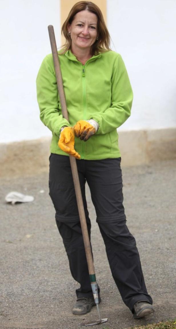 Eine Frau in Arbeitskleidung lehnt sich an eine Gartenhacke.