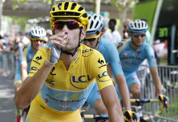 Ein Radrennfahrer in gelbem Trikot trinkt während eines Rennens aus einem Glas.