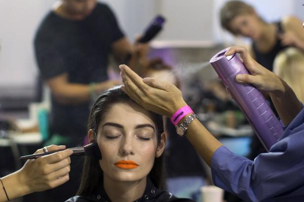 Eine Frau mit geschlossenen Augen wird geschminkt und bekommt Haarspray aufgesprüht.