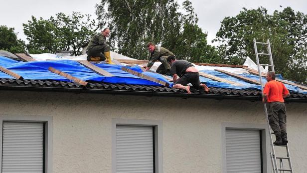 Mehrere Arbeiter reparieren ein mit einer blauen Plane abgedecktes Dach.