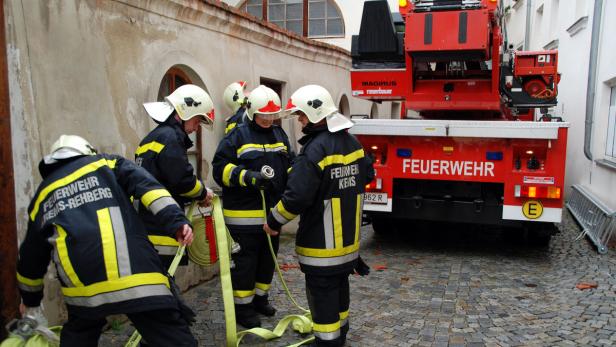 Mehrere Feuerwehrleute hantieren mit einem Schlauch neben einem roten Feuerwehrauto.