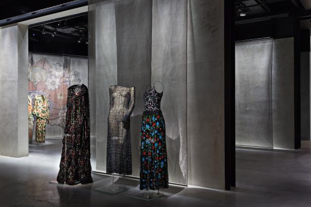 In einer Ausstellung sind drei Kleider auf transparenten Ständern zu sehen.
