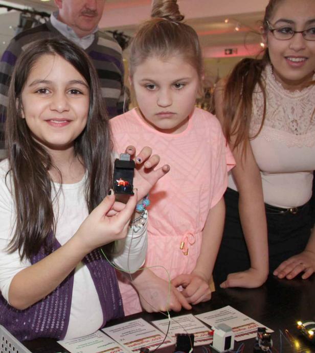 Ein Mädchen hält ein kleines elektronisches Gerät in der Hand, umgeben von anderen Kindern.