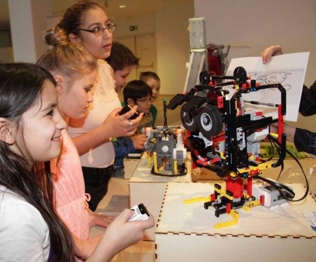 Eine Gruppe Kinder betrachtet und steuert Roboter aus Legosteinen.