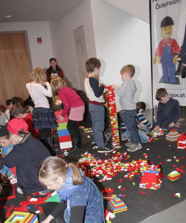 Eine Gruppe Kinder spielt mit bunten Legosteinen in einem Raum.