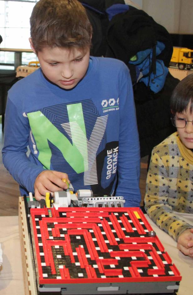 Ein Junge spielt mit einem selbstgebauten Labyrinth aus Legosteinen.