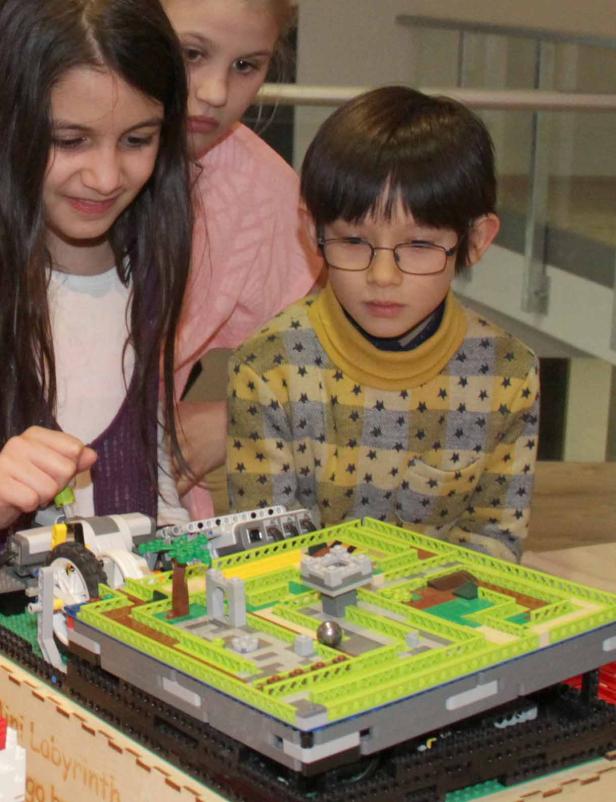 Drei Kinder betrachten ein Mini-Labyrinth aus LEGO-Steinen.