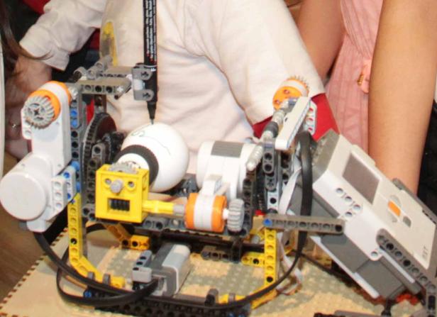 Ein Roboter aus Lego-Steinen zeichnet mit einem Stift auf eine weiße Kugel.