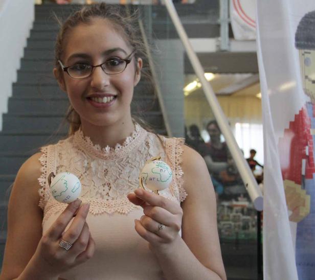 Eine junge Frau hält zwei bemalte Globus-Ornamente in ihren Händen.