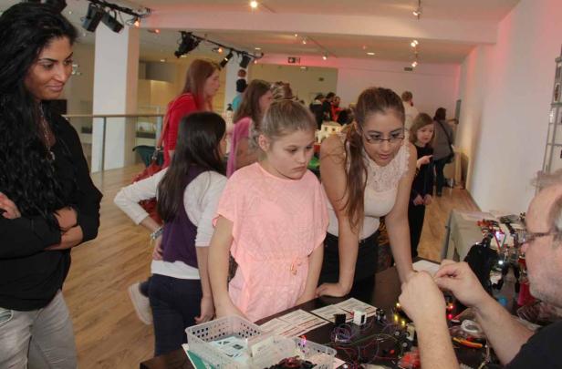 Eine Gruppe von Menschen, darunter Kinder, betrachtet elektronische Bauteile auf einem Tisch.