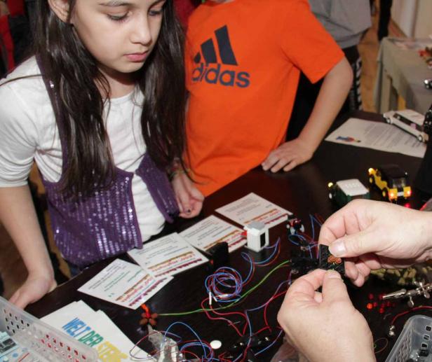 Ein Mädchen und ein Junge beobachten, wie eine Person elektronische Bauteile verbindet.