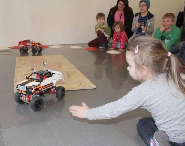 Kinder beobachten ferngesteuerte Monstertrucks aus Lego.