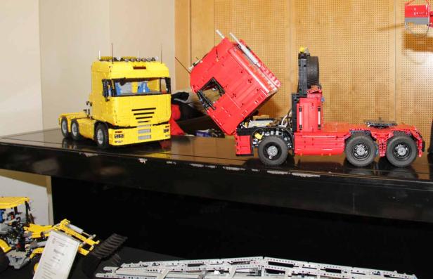 Zwei detailgetreue LKW-Modelle aus Legosteinen, einer gelb und einer rot, stehen auf einem Tisch.