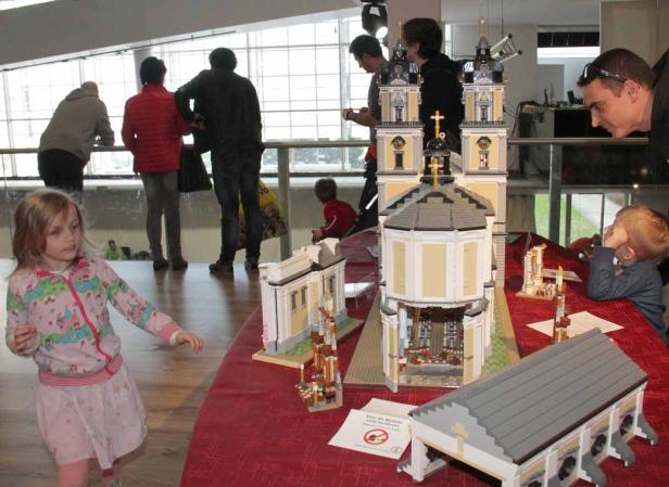 Eine junge Besucherin betrachtet ein detailreiches Kirchenmodell aus Legosteinen.