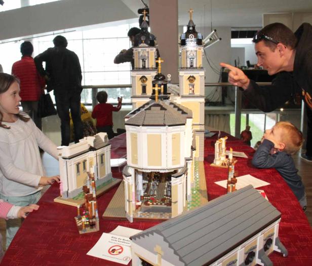 Kinder und ein Mann betrachten ein großes Kirchenmodell aus Legosteinen.