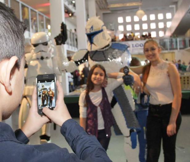 Ein Junge fotografiert mit seinem Smartphone zwei Mädchen und Star Wars Figuren aus Lego.