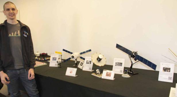 Ein Mann steht neben einem Tisch mit Lego-Modellen von Satelliten.