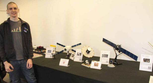Ein Mann steht neben einem Tisch mit Lego-Modellen von Satelliten.