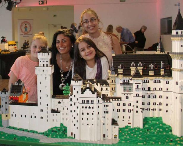 Vier Personen posieren hinter einem Lego-Modell von Schloss Neuschwanstein.