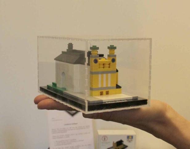 Eine Hand hält ein Lego-Modell einer Kirche in einem transparenten Kasten.