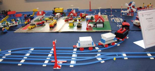 Eine Lego-Eisenbahnlandschaft mit Häusern, Fahrzeugen und einer Windmühle.